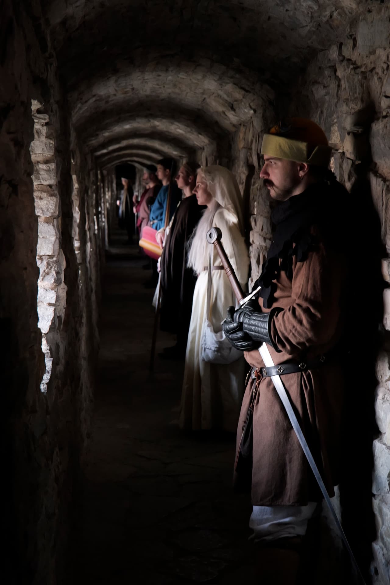 Members in medieval dress standing in a vaulted stone castle passage