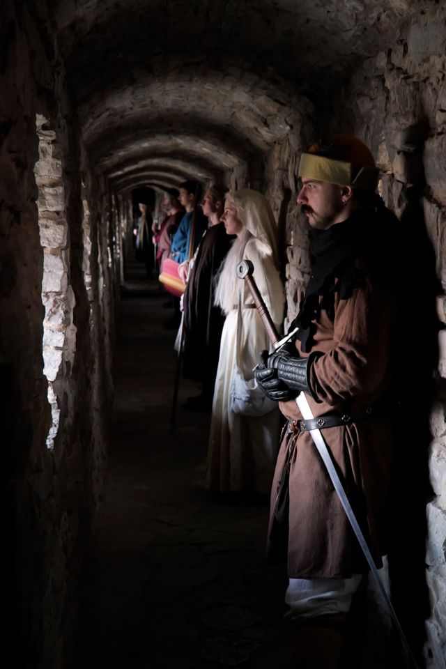 Members in medieval dress standing in a vaulted stone castle passage